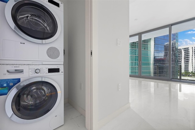 laundry area featuring a view of city, stacked washer and clothes dryer, marble finish floor, laundry area, and baseboards