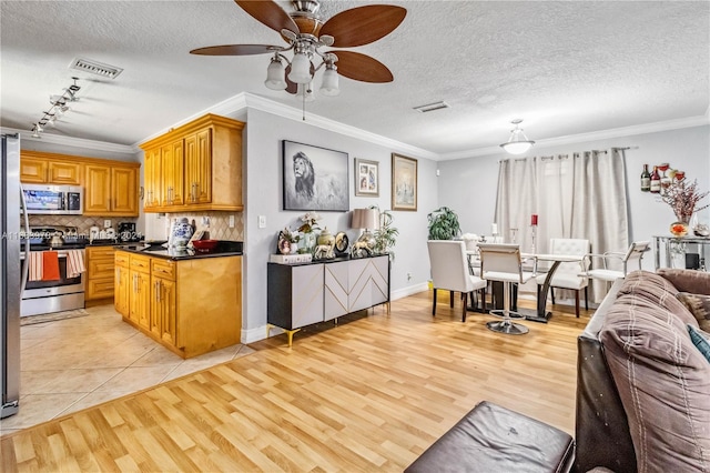 kitchen featuring stainless steel appliances, ornamental molding, light wood-type flooring, a textured ceiling, and ceiling fan