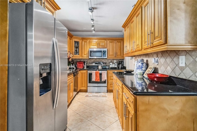 kitchen featuring backsplash, appliances with stainless steel finishes, light tile patterned floors, dark stone counters, and ornamental molding