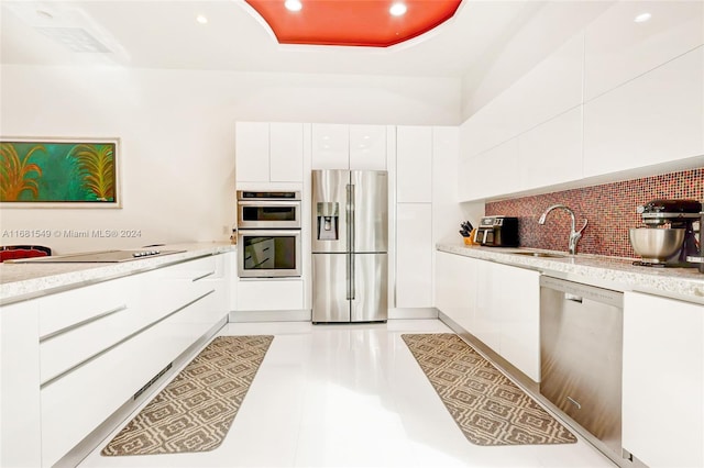 kitchen featuring white cabinets, light tile patterned floors, appliances with stainless steel finishes, backsplash, and sink