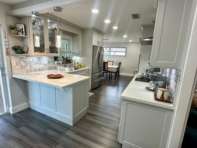 kitchen featuring kitchen peninsula, stainless steel fridge, dark hardwood / wood-style flooring, white cabinetry, and hanging light fixtures