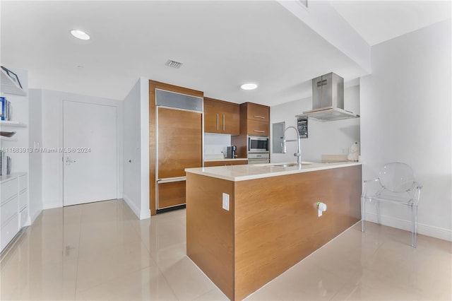 kitchen with wall chimney range hood, kitchen peninsula, light tile patterned flooring, built in appliances, and sink