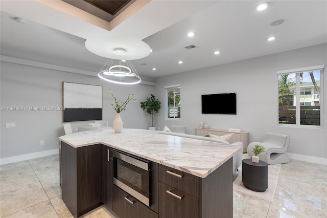 kitchen with pendant lighting, dark brown cabinets, stainless steel microwave, and a healthy amount of sunlight