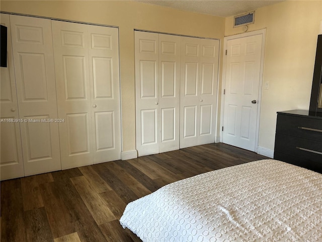 bedroom with dark wood-type flooring, two closets, and a textured ceiling