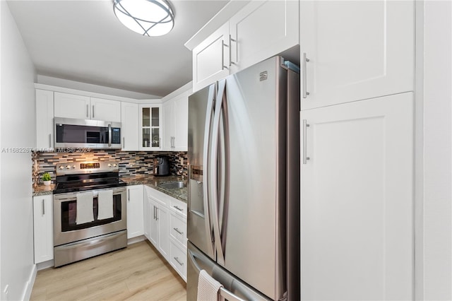 kitchen featuring light hardwood / wood-style floors, appliances with stainless steel finishes, white cabinets, and dark stone countertops