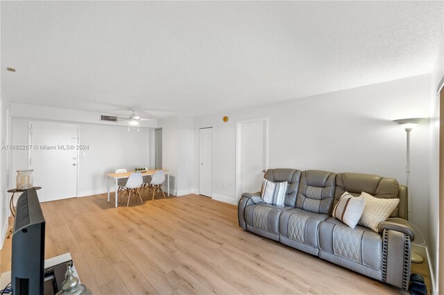 living room featuring light hardwood / wood-style floors, a textured ceiling, and ceiling fan