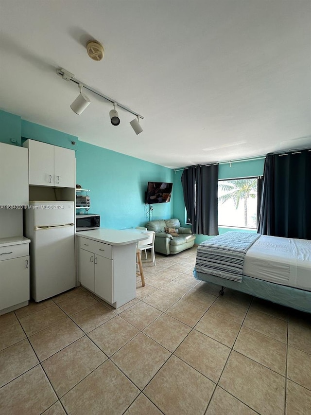 unfurnished bedroom featuring rail lighting, light tile patterned floors, and white fridge