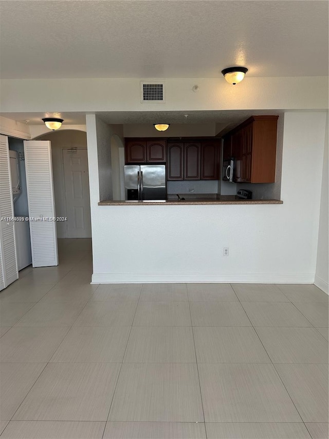 kitchen with appliances with stainless steel finishes, dark brown cabinets, a textured ceiling, kitchen peninsula, and light tile patterned floors