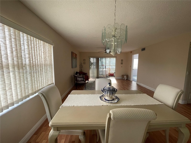 dining room with wood-type flooring, a textured ceiling, and ceiling fan with notable chandelier