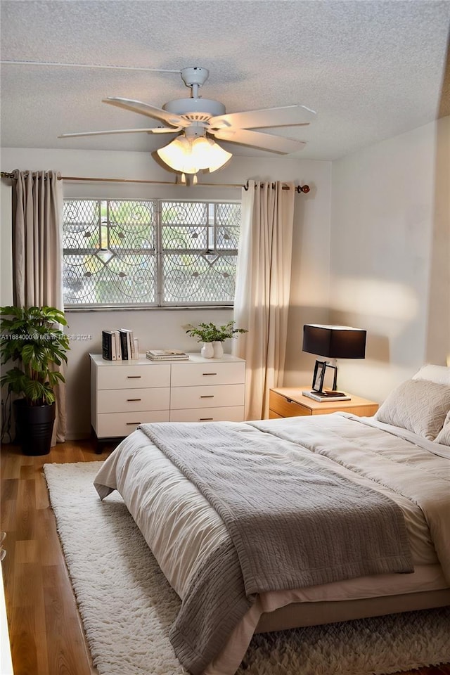 bedroom with ceiling fan, hardwood / wood-style flooring, a textured ceiling, and multiple windows