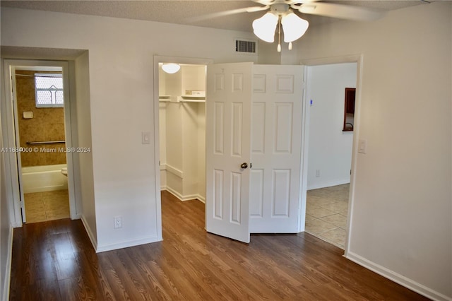 unfurnished bedroom featuring a spacious closet, a textured ceiling, a closet, ceiling fan, and dark wood-type flooring