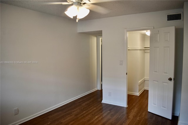 unfurnished bedroom featuring dark hardwood / wood-style flooring, a walk in closet, ceiling fan, a textured ceiling, and a closet