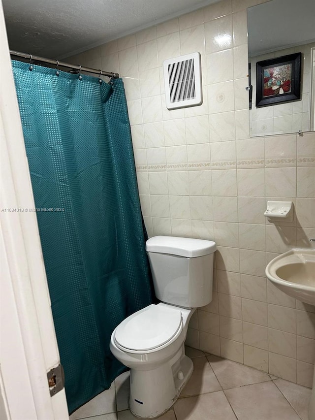 bathroom featuring a textured ceiling, toilet, tile walls, walk in shower, and tile patterned flooring