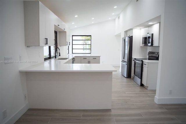 kitchen with lofted ceiling, kitchen peninsula, stainless steel appliances, sink, and white cabinets