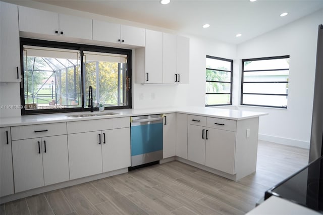 kitchen featuring lofted ceiling, dishwasher, kitchen peninsula, sink, and white cabinets