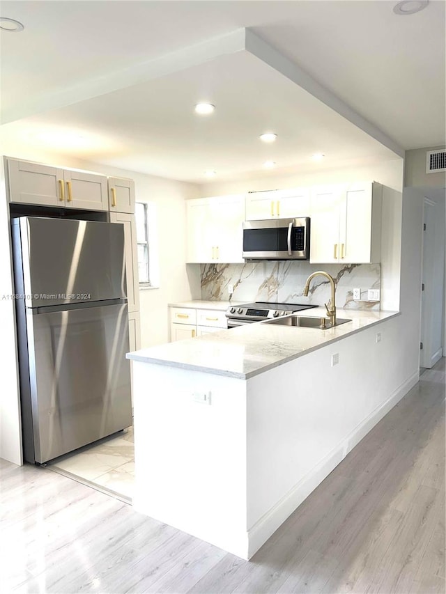 kitchen featuring stainless steel appliances, kitchen peninsula, white cabinets, light wood-type flooring, and decorative backsplash