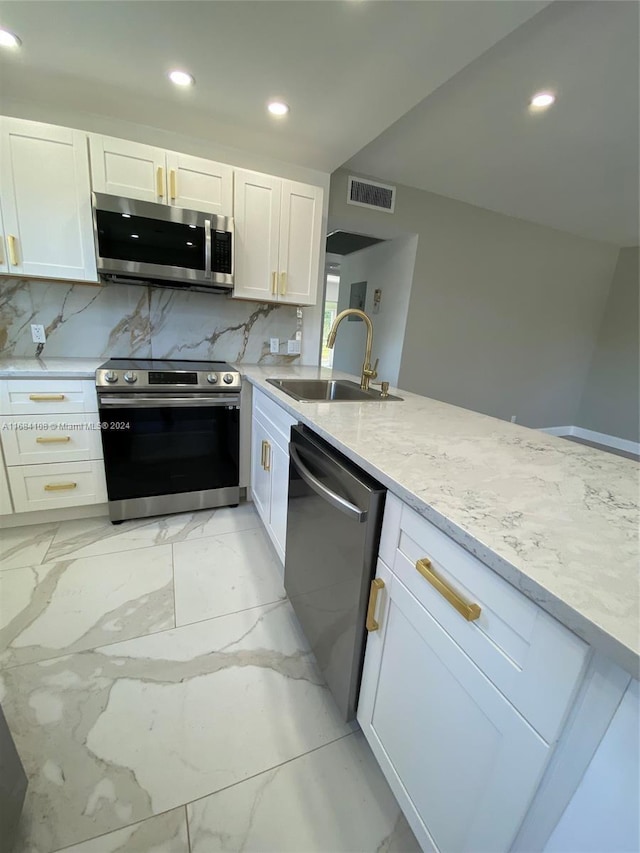 kitchen with tasteful backsplash, light stone counters, appliances with stainless steel finishes, sink, and white cabinets