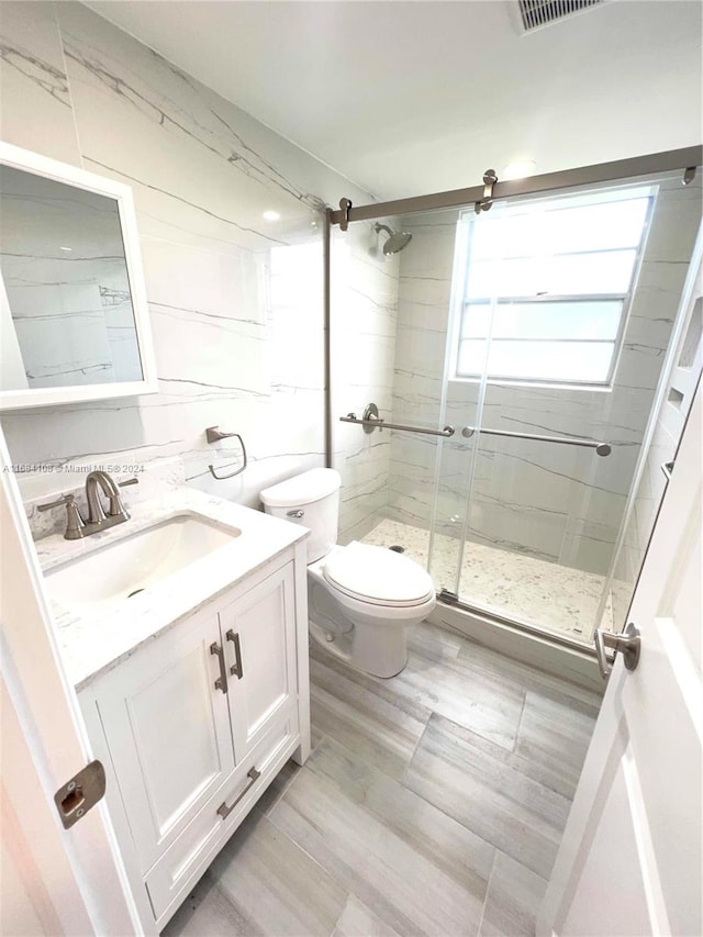 bathroom featuring toilet, vanity, and a shower with shower door