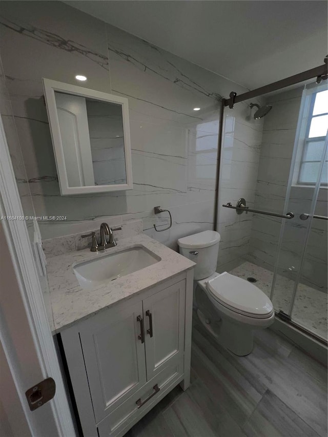 bathroom with tile walls, an enclosed shower, vanity, and toilet