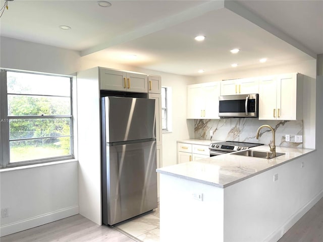 kitchen with stainless steel appliances, white cabinetry, sink, kitchen peninsula, and light stone countertops