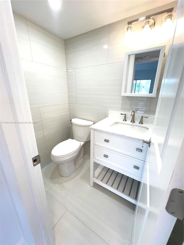 bathroom featuring toilet, vanity, tile patterned flooring, and tile walls