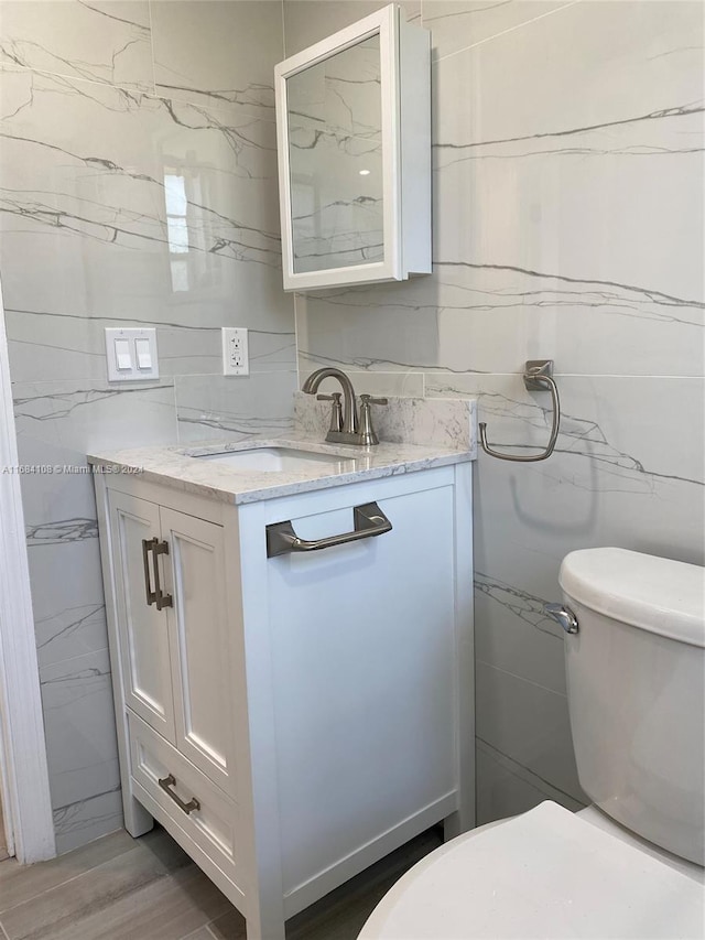 bathroom with toilet, vanity, and tile walls