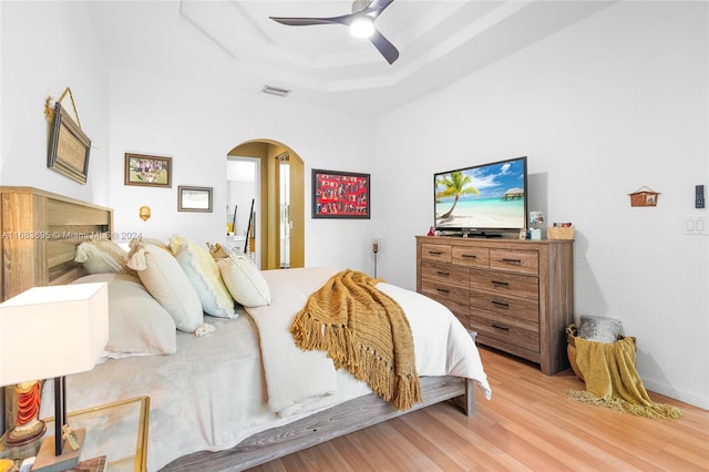 bedroom with light hardwood / wood-style floors, a raised ceiling, and ceiling fan