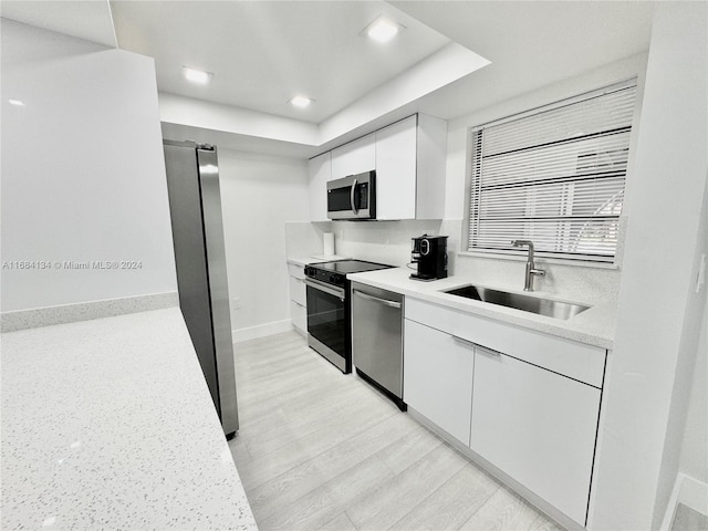 kitchen featuring appliances with stainless steel finishes, white cabinetry, sink, and light hardwood / wood-style floors