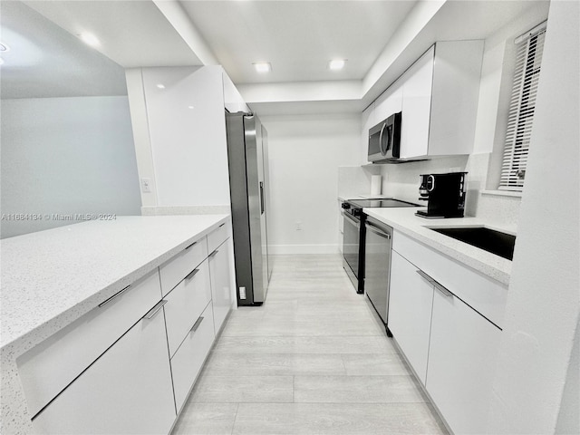 kitchen with appliances with stainless steel finishes, white cabinetry, sink, and light hardwood / wood-style floors