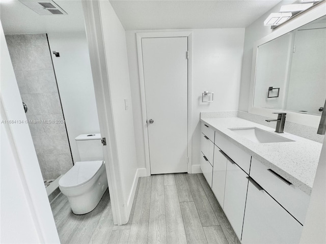 bathroom with toilet, hardwood / wood-style flooring, vanity, and tiled shower