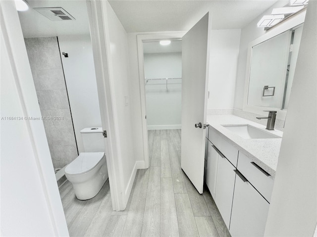 bathroom with vanity, toilet, hardwood / wood-style flooring, and tiled shower