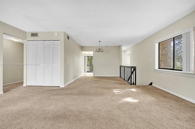 spare room featuring a chandelier, a textured ceiling, and carpet flooring