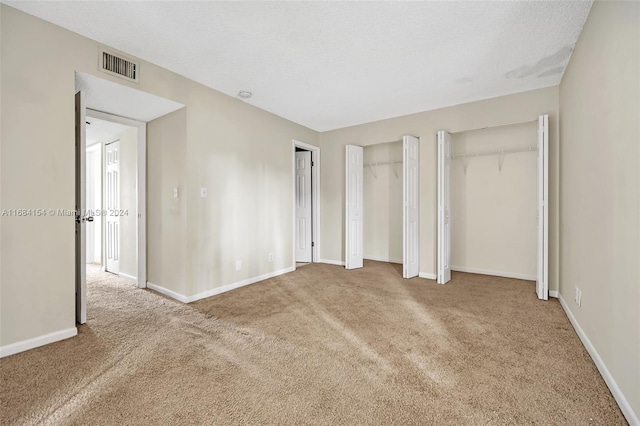 unfurnished bedroom with a textured ceiling, carpet flooring, and two closets