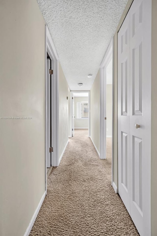 hallway with a textured ceiling and light carpet