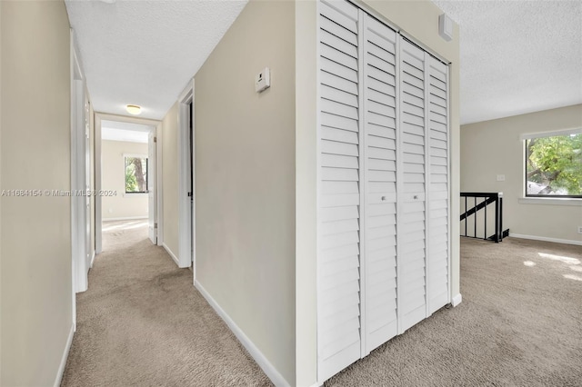 corridor featuring a textured ceiling and light carpet