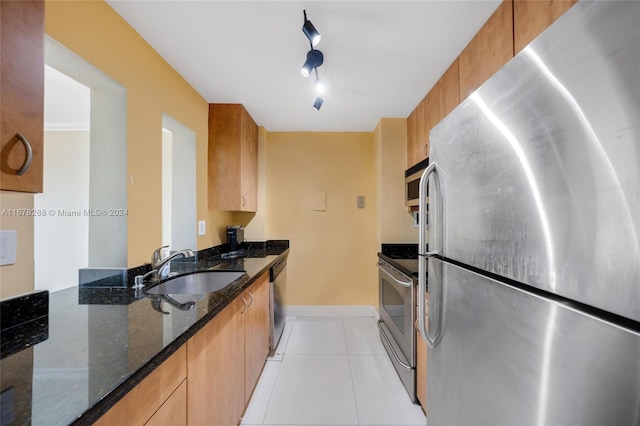 kitchen with track lighting, stainless steel appliances, dark stone counters, sink, and light tile patterned floors