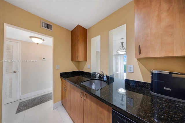 kitchen featuring sink, light tile patterned flooring, hanging light fixtures, and dark stone countertops