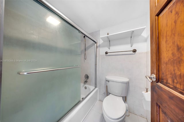 bathroom with tile walls, enclosed tub / shower combo, toilet, and tile patterned flooring