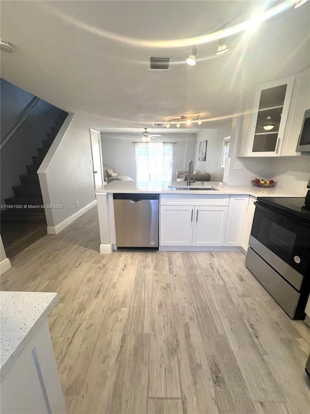 kitchen with appliances with stainless steel finishes, sink, light wood-type flooring, white cabinetry, and ceiling fan