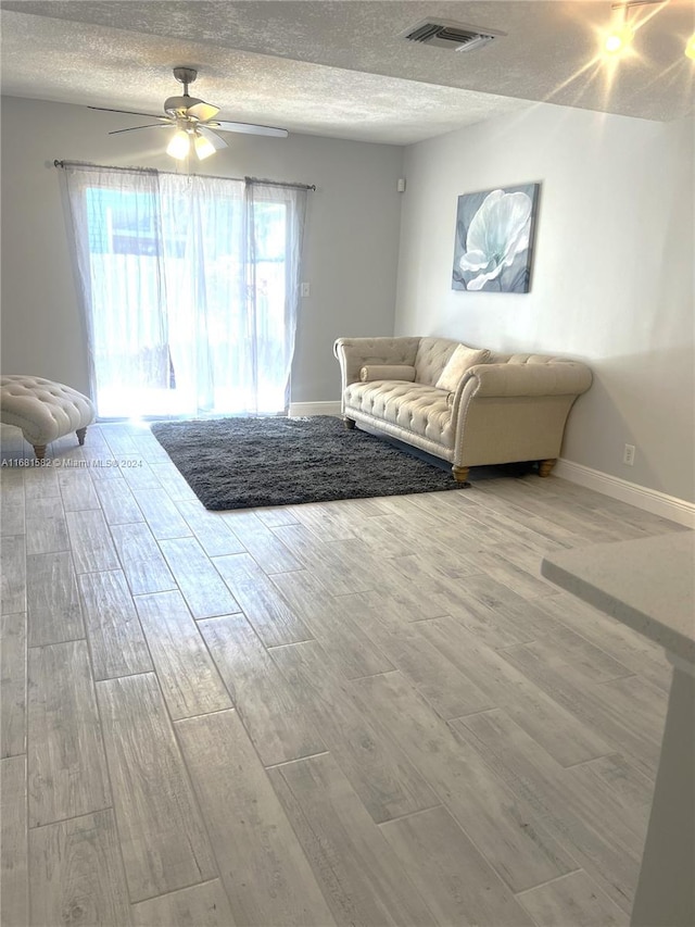 living room with a textured ceiling, light wood-type flooring, and ceiling fan