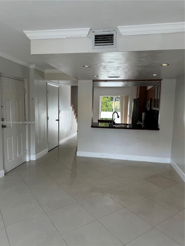 unfurnished living room featuring sink, crown molding, and light tile patterned floors