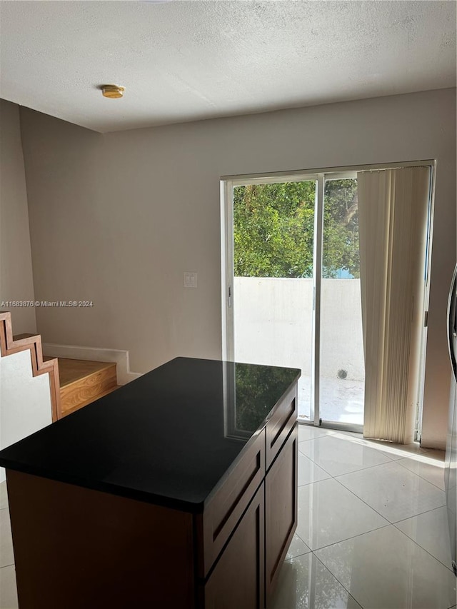 kitchen featuring a textured ceiling, dark brown cabinetry, a kitchen island, and light tile patterned floors