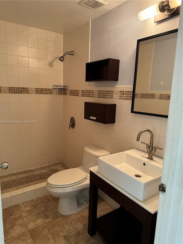 bathroom with toilet, vanity, a tile shower, and tile walls