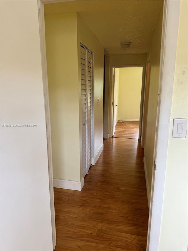 hallway with a textured ceiling and wood-type flooring