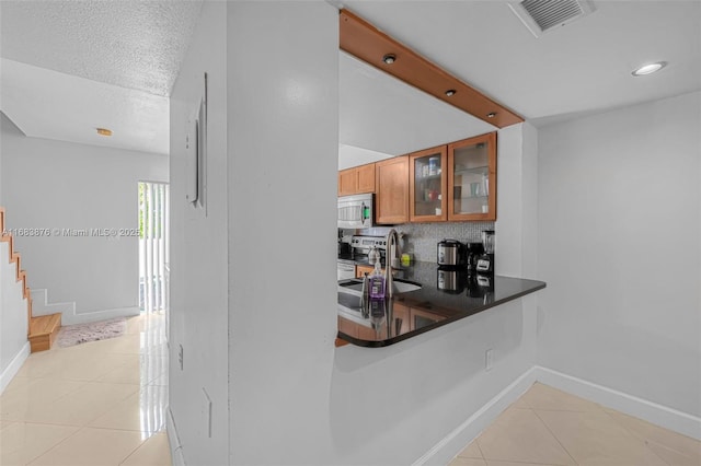 kitchen featuring a sink, appliances with stainless steel finishes, decorative backsplash, light tile patterned floors, and baseboards