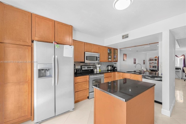 kitchen featuring appliances with stainless steel finishes, a sink, dark countertops, backsplash, and light tile patterned floors