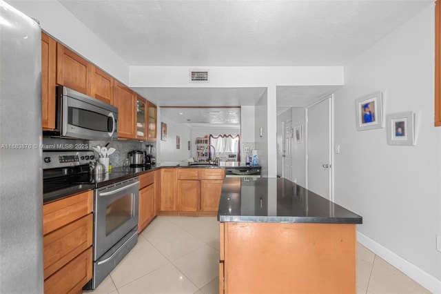 kitchen with appliances with stainless steel finishes, light tile patterned flooring, a center island, a sink, and tasteful backsplash
