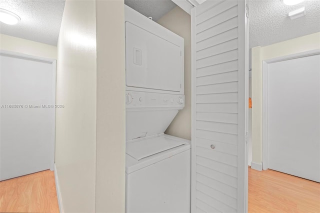 laundry area with estacked washer and dryer, a textured ceiling, and light wood finished floors