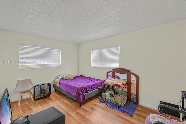 bedroom with a textured ceiling, wood finished floors, and baseboards