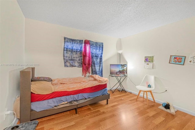 bedroom featuring wood finished floors, a textured ceiling, and baseboards